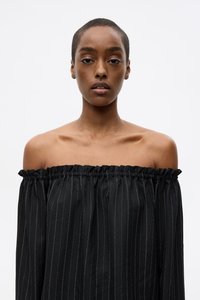 Off-the-shoulder svart topp med vertikale hvite striper, med en rynket halslinje og jevn tekstur. Enkel design uten mønstre.