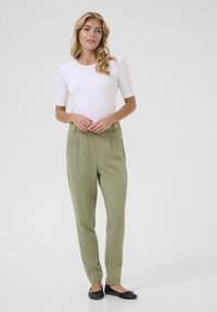Un haut blanc à manches courtes associé à un pantalon plissé vert olive et des ballerines noires. La tenue présente un design simple et épuré avec des textures lisses.