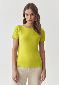 Kortærmet, rundhalset, lys limegrøn t-shirt lavet af glat stof. Båret med lyse, beige linnedbukser; minimal tekstur og design.