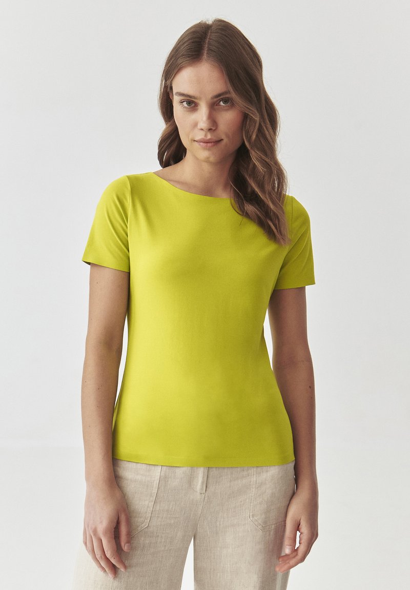 Kortærmet, rundhalset, lys limegrøn t-shirt lavet af glat stof. Båret med lyse, beige linnedbukser; minimal tekstur og design.