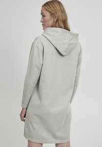 Hellgraues Kapuzen-Sweatkleid mit langen Ärmeln, strukturiertem Stoff und lockerer Passform, das bis zur Mitte des Oberschenkels reicht. Verstellbare Kapuzendetails.