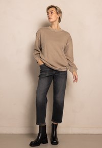 Beige oversized sweatshirt, dark denim jeans, and black ankle boots. Smooth texture, relaxed fit, and mid-rise waist. Simple design.