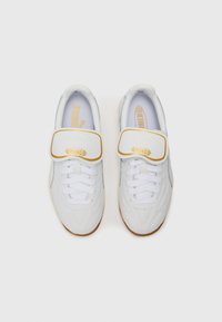 Witte sportschoenen met een soepele synthetische bovenkant, voorzien van een klittenbandsluiting en een gestructureerde rubberen zool. Gouden en blauwe accenten op de branding.