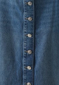 Jeansklänning med knäppning fram som har silverfärgad detalj, i medelblått tyg med en texturerad yta och en klassisk tvätteffekt.