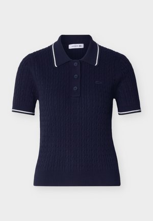 Polo de punto de cable azul marino de manga corta con ribete blanco en el cuello y las mangas, tres botones y logo de Lacoste en el pecho.