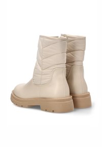 Botas de tobillo beige con un acabado de cuero liso y acentos de textil acolchado. Suela de goma gruesa. Cierre de cremallera en la parte trasera para facilitar el uso.