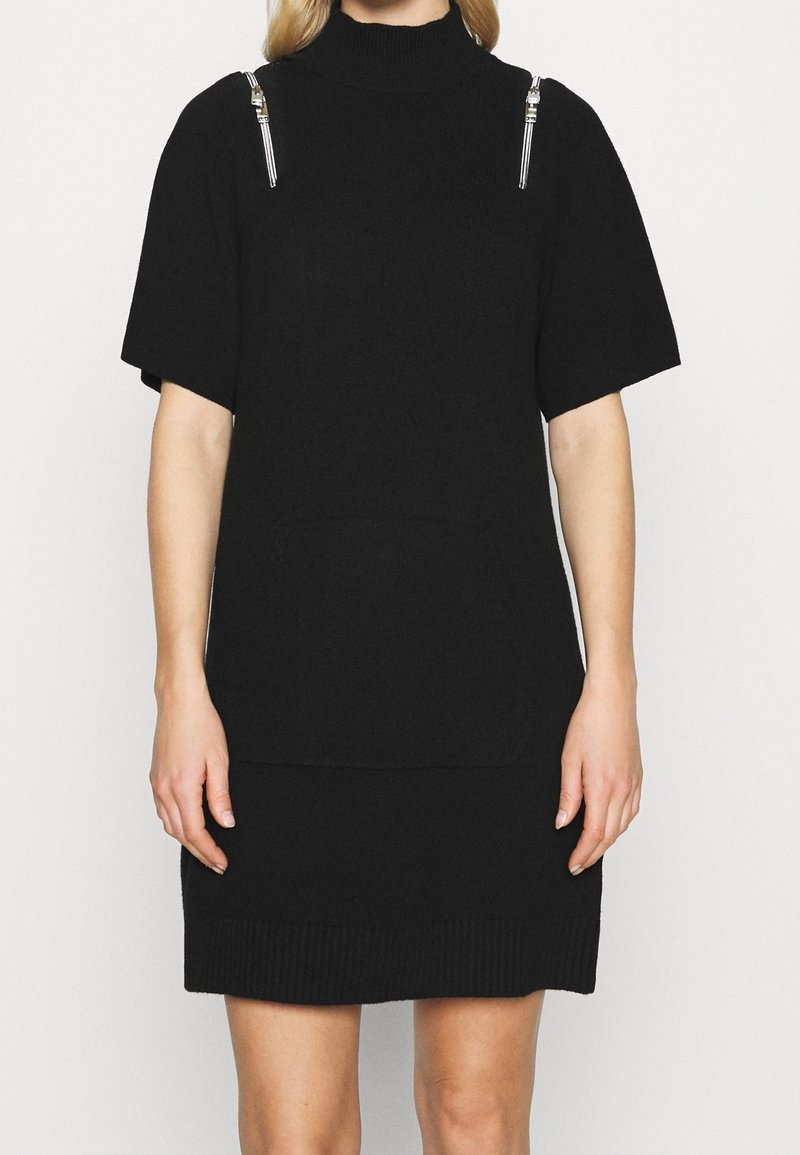 Robe en maille noire à manches courtes, col montant et coupe ample. Présente des accents de quincaillerie argentée sur les épaules et une poche avant.