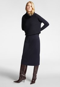 Maglione blu navy con righe testurizzate, collo alto, abbinato a una gonna a tubo blu navy e stivali al ginocchio in pelle di coccodrillo bordeaux lucidi.