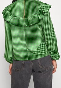 Green gingham blouse with ruffled back accent, long sleeves, and a keyhole closure. Fabric has a smooth texture with a fitted waist.