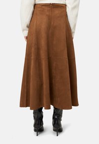Barna szarvasbőr maxi szoknya bővülő szabással, varrásdíszítéssel és hátul rejtett cipzárral. Puha textúra, A-vonalú sziluett.
