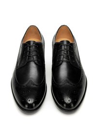Czarne oksfordki ze skóry licowej o gładkiej powierzchni, zdobione szczegółowym wzorem brogue, zaokrąglonym noskiem i z przodu sznurowane. Wnętrze wyściełane beżową podszewką.