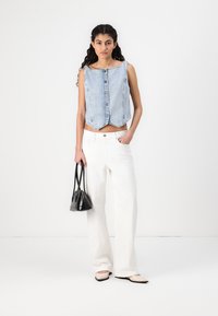 Chaleco de mezclilla azul claro, recortado y con escote cuadrado, con cierre de botones en el frente, combinado con pantalones de pierna ancha blancos de cintura alta y un pequeño bolso negro.