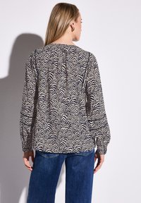 Långärmad blus med ett krämfärgat och marinblått vågigt mönster, lätt tyg, rundad halsringning, veckat bakstycke och avslappnad passform. Kombination med blå jeans.