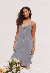 Stribet kjole med tynde stropper, knapper foran og en skørt med vidde. Farverne er marineblå og hvid. Glat stof med en afslappet pasform.