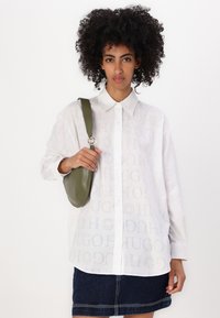 White shirt with subtle "HUGO" pattern, long sleeves, button-up design. Paired with a green leather crossbody bag. Denim skirt.