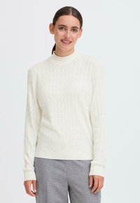 White knitted sweater with a high neckline and a textured diamond pattern. Features long sleeves and a fitted design.
