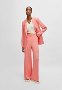 Pink suit featuring a fitted blazer and wide-leg trousers, paired with a cream top. Smooth texture with no visible patterns or embellishments.
