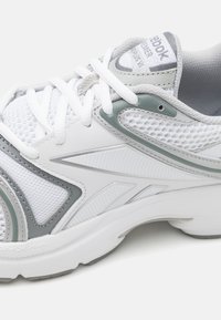 Sapatilha atlética branca com acentos cinzentos, tecido em malha, sobreposições texturizadas e sola acolchoada, apresentando atacadores e a marca "Reebok".