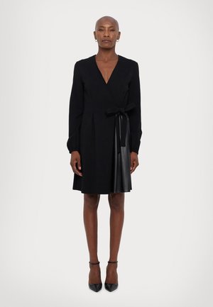 Black wrap dress with long sleeves, featuring a satin tie at the waist and a leather-like skirt. Smooth texture and tailored design.