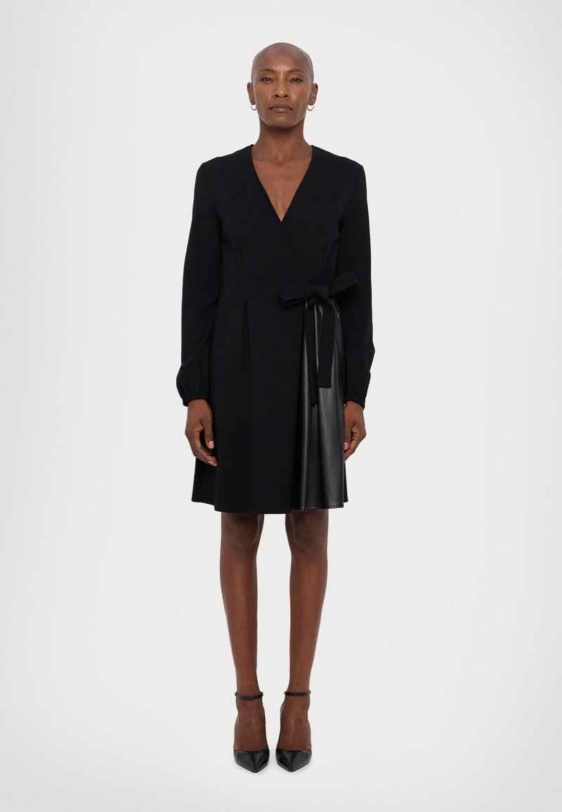 Schwarzes Wickelkleid mit langen Ärmeln, ausgestattet mit einem satinierten Gürtel in der Taille und einem lederähnlichen Rock. Glatte Textur und maßgeschneidertes Design.