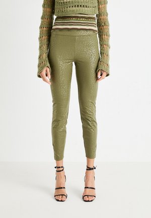 Leggings aderenti verde oliva con stampa leopardata testurizzata. Design a vita alta, abbinati a tacchi neri con cinturini, che esaltano la silhouette snella.