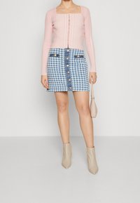Haut à manches longues côtelé rose clair avec décolleté carré, associé à une jupe en denim à motif pied-de-poule bleu comportant des boutons sur le devant et des bottines beige.