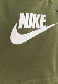 Olivgrön sweatshirt gjord av ett tyg med en slät textur, präglad av en stor vit Nike-logotyp och swoosh-design på framsidan.