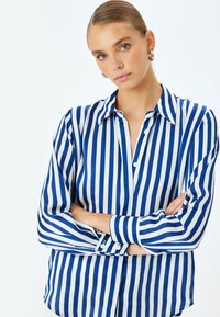 Camicia a righe con bottoni, caratterizzata da strisce verticali blu e bianche, colletto e maniche lunghe con polsini abbottonati, realizzata in tessuto liscio.