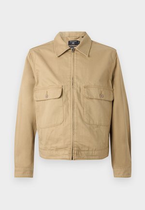 Tan, cotton jacket with a straight cut, pointy collar, front zipper closure, and two chest pockets with button flaps.