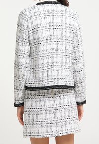 Giacca tweed bianca e nera con un motivo a quadri tessuto, rifiniture nere e un design aderente, abbinata a una mini gonna coordinata.