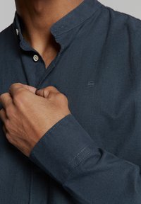 Navyblauw overhemd met kraag, gemaakt van zachte stof en voorzien van een knoopsluiting. Het shirt heeft een subtiele textuur en stikaccenten op de manchetten.
