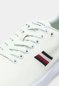 Witte sneaker van textiel met structuur, voorzien van het kenmerkende Tommy Hilfiger-logo in rood, wit en blauw. Inclusief witte veters en oogjes.