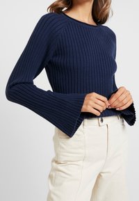 Marinblå ribbad tröja med en figurnära passform och utsvängda ärmar, tillverkad av mjukt stickat material. Kombination med ljusbeige högmidjade byxor.