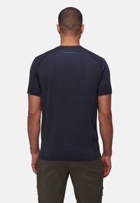 Kungsblå t-shirt med kort ärm, tillverkad av stretchigt material, med en slät yta och reflekterande logotyp på baksidan. Avslappnad passform, minimalistisk design.