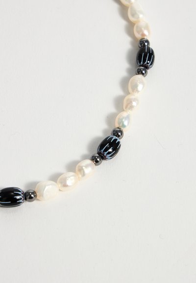 Chapelet de perles blanches irrégulières alternant avec de petites perles noires, certaines perles noires sont ovales avec des motifs de rayures ondulées bleues.