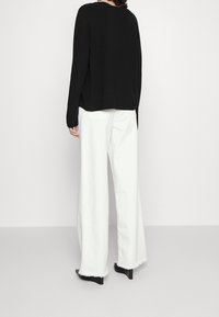 Zwarte gebreide trui met een relaxte pasvorm, gecombineerd met witte jeans met wijde pijpen, afgewerkt met rafelige zomen en achterzakken, gedragen met schoenen met hakken.