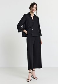 Blusa nera con bordi in pizzo sulle maniche a campana, abbinata a pantaloni neri a gamba larga e sandali neri con tacco alto e cinturini. Tessuto dal tocco morbido.