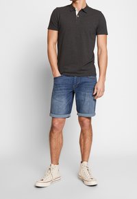 Polo gris foncé avec col blanc, associé à un short en denim bleu avec revers, et des baskets montantes blanches.