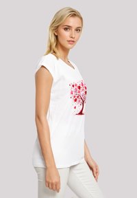 White cotton T-shirt featuring a red and pink heart tree graphic. Short sleeves and a relaxed fit. Smooth texture, minimalistic design.