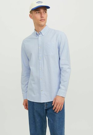 Light blue and white striped button-down shirt with a chest pocket, long sleeves, and light fabric texture, worn with blue denim pants.