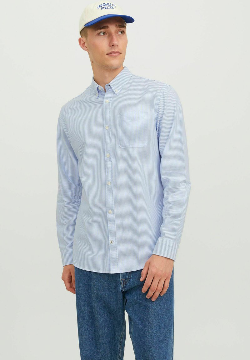 Hellblau und weiß gestreiftes Button-Down-Hemd mit einer Brusttasche, langen Ärmeln und leichter Stofftextur, getragen mit blauen Jeanshosen.