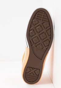 Oranžové plátěné tenisky s bílou gumovou podrážkou, které mají texturovanou hnědou podešev a branding Converse. Pruhované akcenty v bílé a světle fialové barvě.