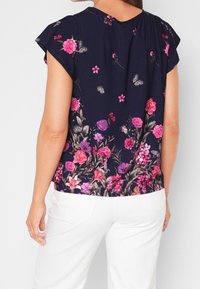 Mörkblå kortärmad blus med ett blomstertryck i rosa och lila nyanser, med en ledig design och rynkade detaljer på ryggen.