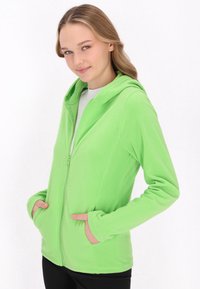 Felpa verde con zip e design aderente, dotata di zip frontale, due tasche laterali e cappuccio. Texture morbida.