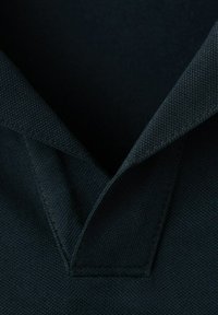 Primer plano de un cuello de tela oscura con abertura en forma de V, mostrando el tejido texturizado y detalles de costura.