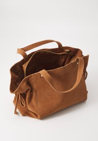 Sac en daim brun avec un espace intérieur spacieux, fermeture éclair et deux poignées souples, arborant un design décontracté et de subtils détails de couture.