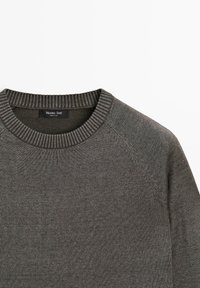Ciemnoszary sweter dzianinowy z okrągłym dekoltem, z żebrowanym kołnierzem i rękawami typu raglan, z czarną metką marki wewnątrz kołnierza.