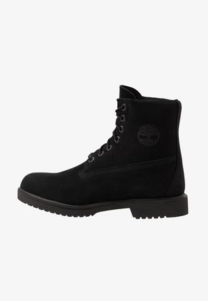 Bota negra de tobillo con cordones, suela gruesa y logotipo en relieve de árbol en el lateral, fabricada con material de cuero mate.
