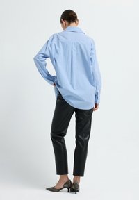 Modrá a bílá pruhovaná oversized košile s špičatým límcem, kombinovaná s černými kalhotami z umělé kůže a kovovými botami na podpatku.