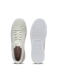 Puma-Sneaker mit einem hellbeigen Obermaterial, rosa Akzenten und einer strukturierten weißen Gummisohle. Die Schnürsenkel und das Branding auf der Zunge sind sichtbar.
